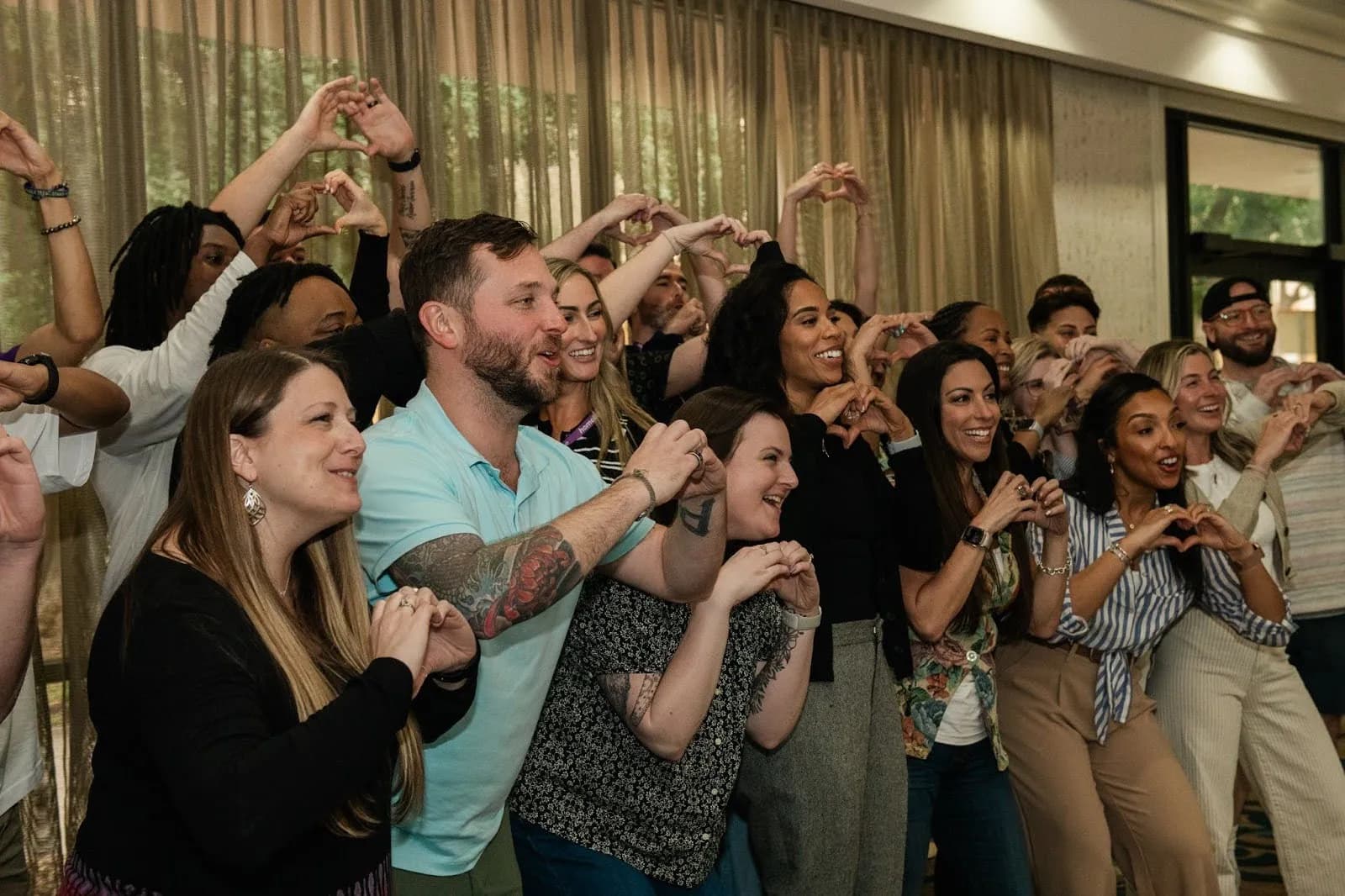 Group of diverse people smiling and making heart shapes with their hands indoors.