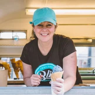 A smiling employee in a teal cap holding an ice cream cone at an ice cream truck service window