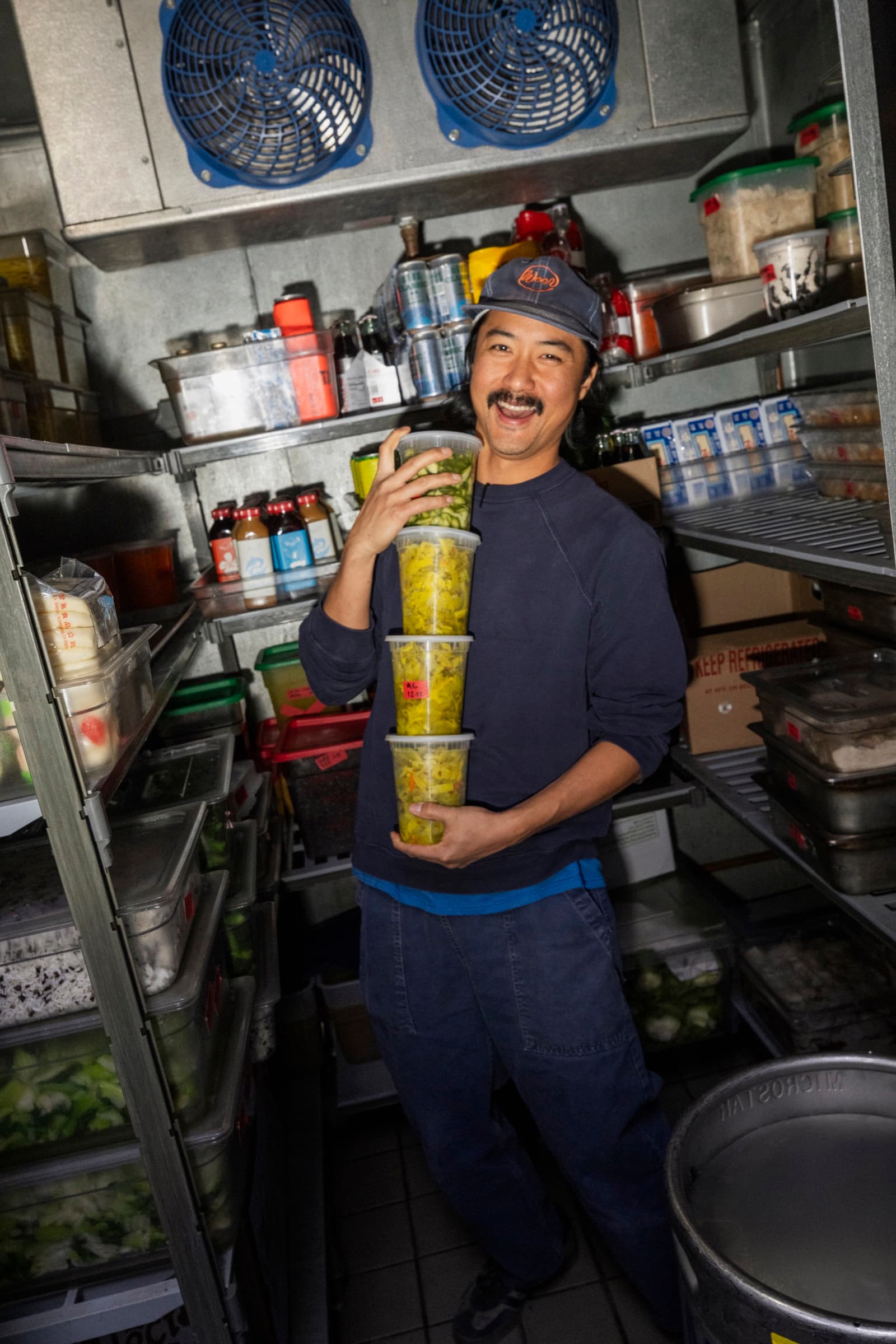Keegan Fong, owner of Woon, holding stacked containers of pickled vegetables.