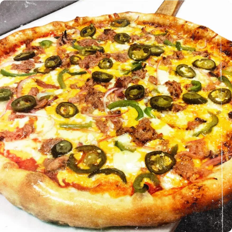 Close-up of a pizza with cheese, jalapeño slices, green bell peppers, red onions, and chunks of meat on a thick crust.