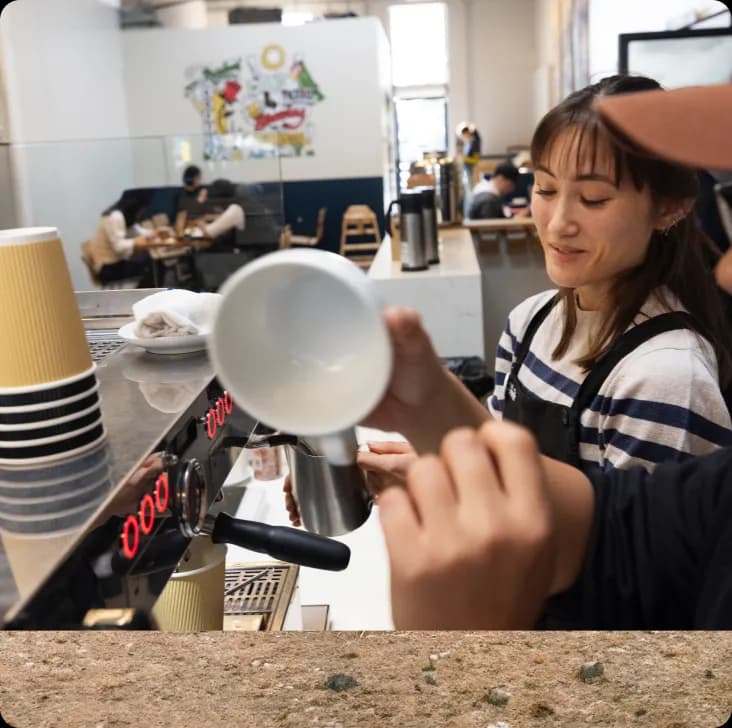 Barista in a dark apron steaming milk behind an espresso machine.
