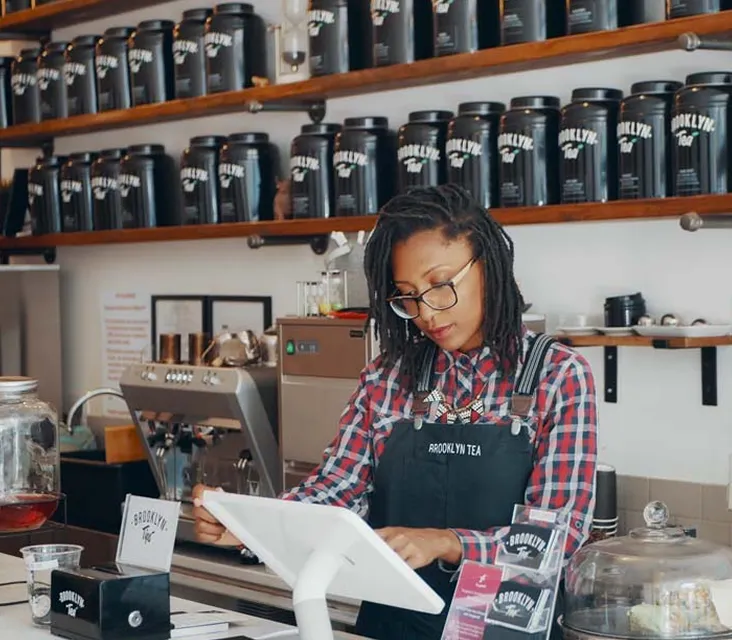 Brooklyn Tea team member pouring loose-leaf tea behind the shop counter.