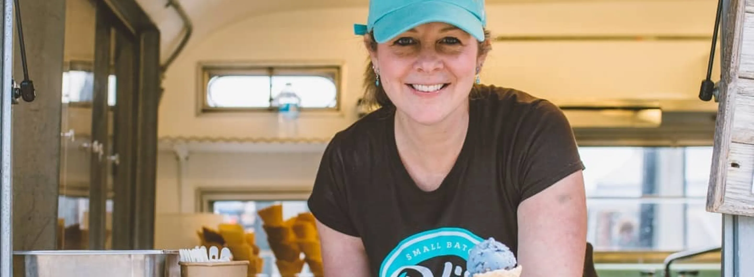 A lady in matching blue hat with black shirt that reads "small batch"