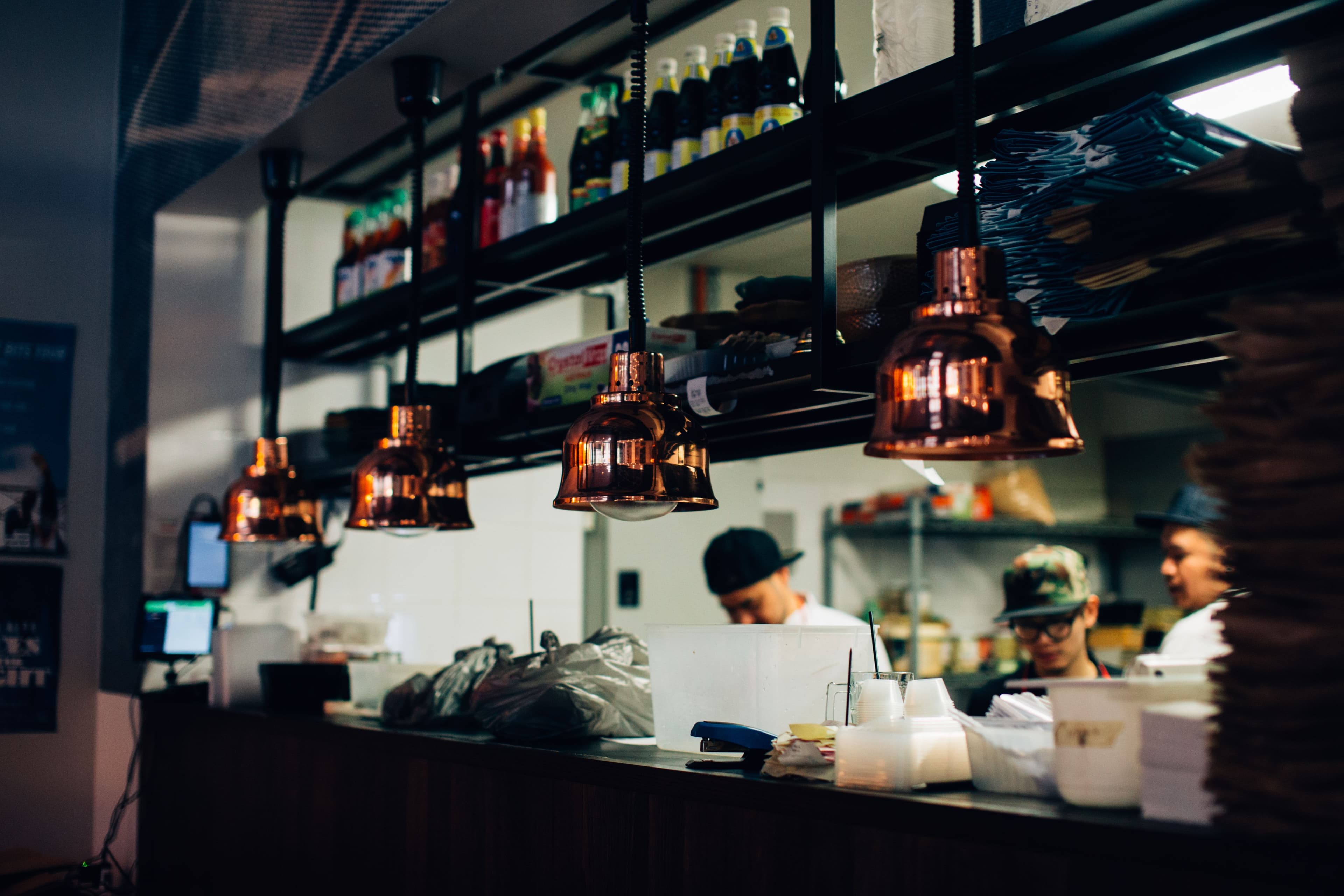 Restaurant kitchen crew working behind a pass counter beneath copper heat lamps.