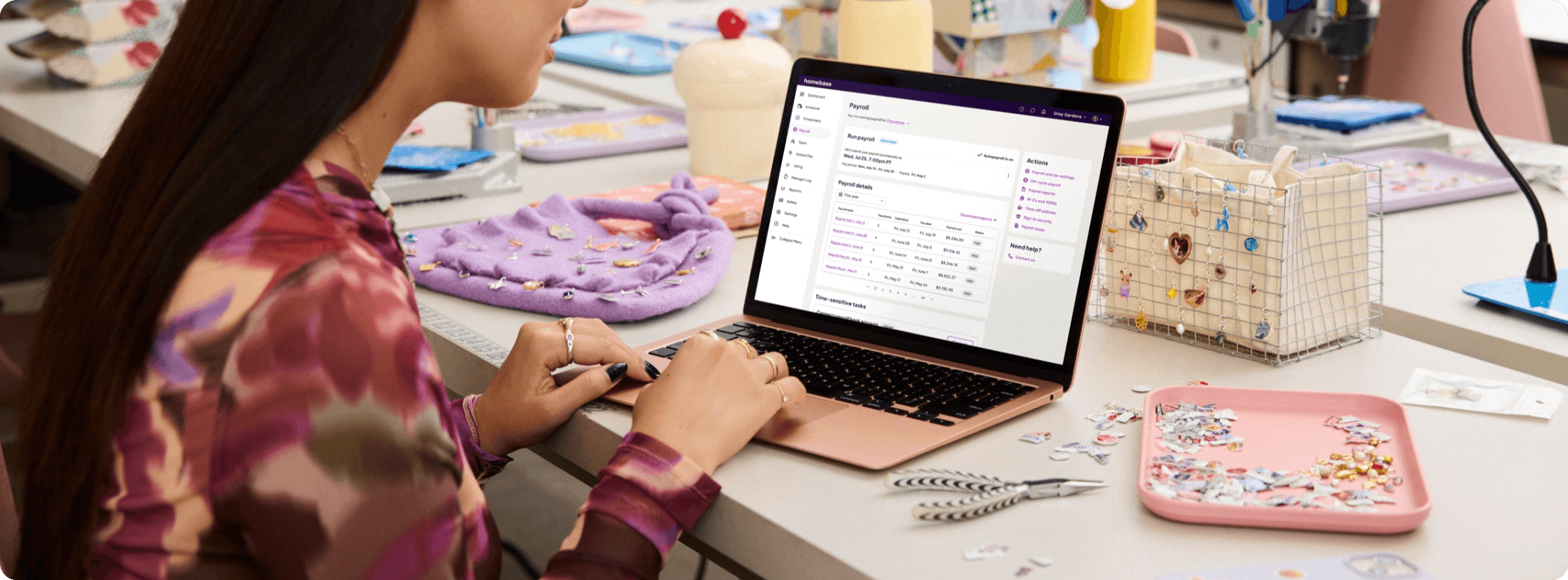 Small business owner at a craft shop table running Homebase payroll on her laptop