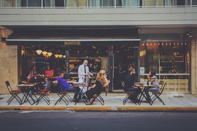 tables on the sidewalk with people eating