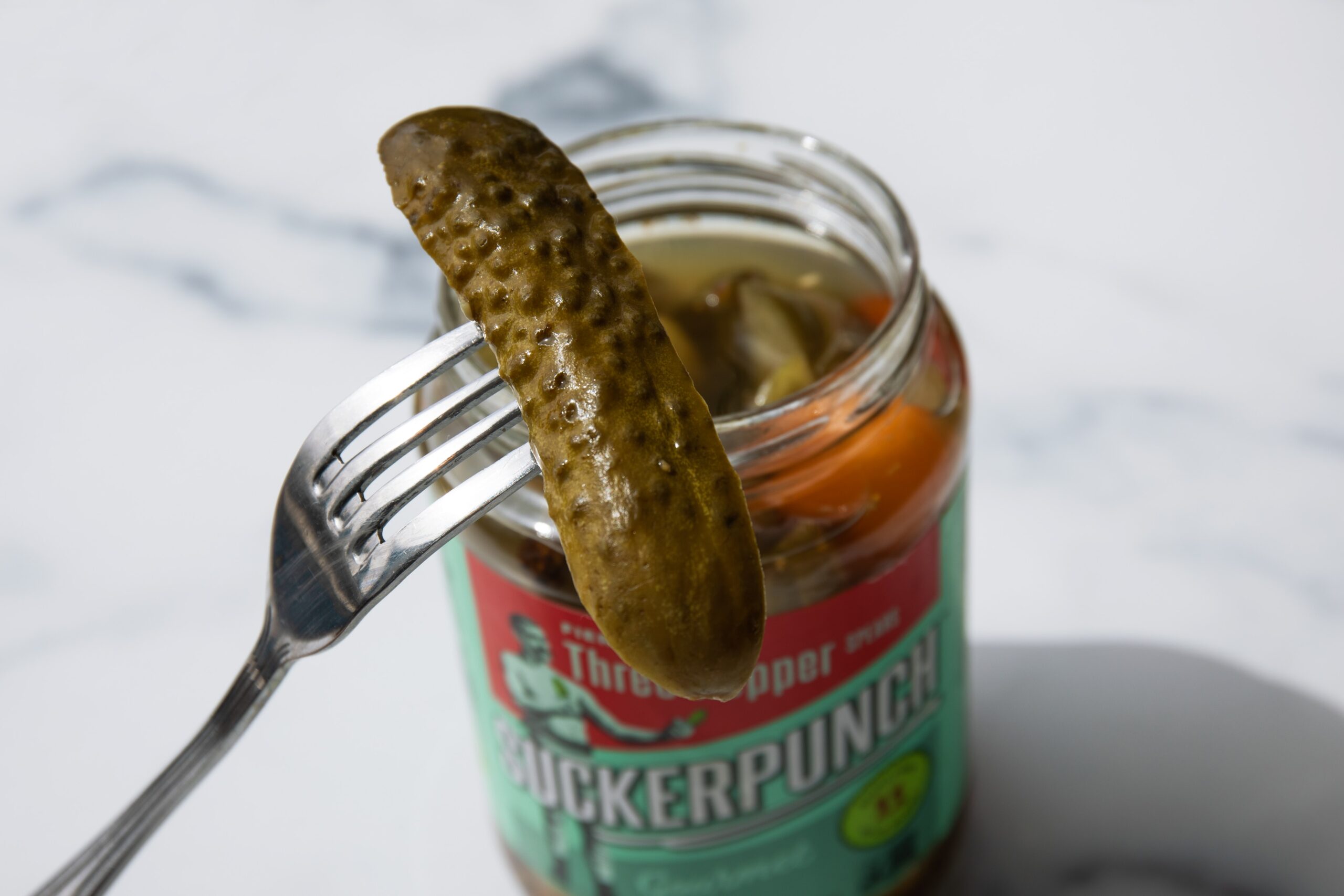 fork holding a pickle in front of jar